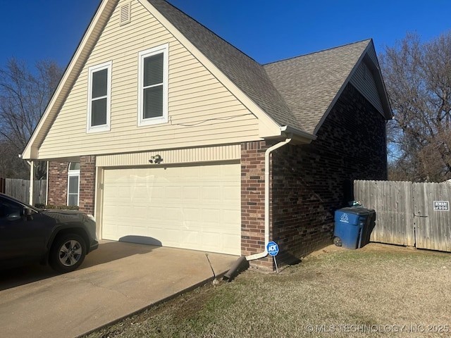 view of side of property with a garage, brick siding, fence, concrete driveway, and roof with shingles