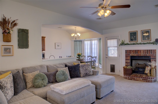 carpeted living area with lofted ceiling, a brick fireplace, visible vents, and ceiling fan with notable chandelier