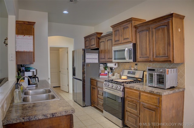 kitchen with light tile patterned floors, a toaster, appliances with stainless steel finishes, a sink, and backsplash