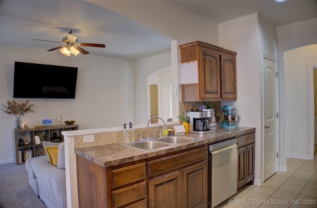 kitchen with arched walkways, brown cabinetry, a ceiling fan, dishwasher, and a sink