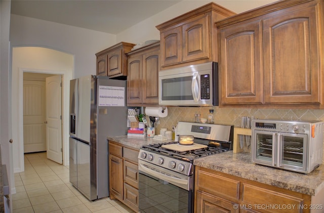 kitchen featuring arched walkways, a toaster, light tile patterned floors, stainless steel appliances, and decorative backsplash