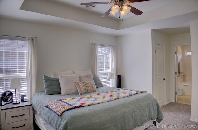 bedroom with a tray ceiling, visible vents, ensuite bath, and carpet