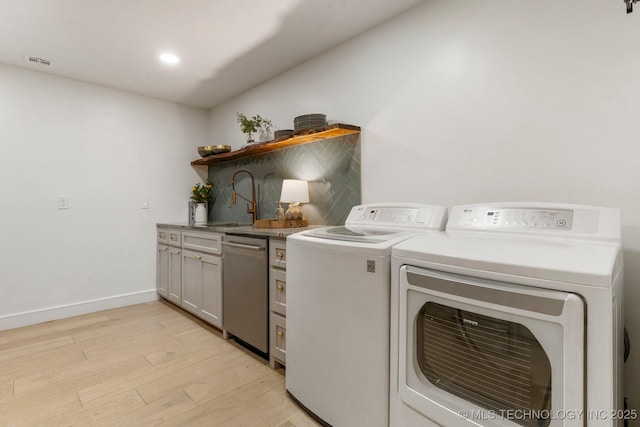 clothes washing area featuring baseboards, visible vents, light wood-type flooring, separate washer and dryer, and a sink