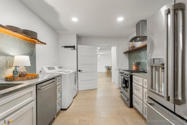 kitchen with separate washer and dryer, high quality appliances, wall chimney exhaust hood, light wood-type flooring, and open shelves