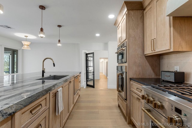 kitchen featuring light wood-style flooring, dark stone countertops, a sink, stainless steel appliances, and backsplash