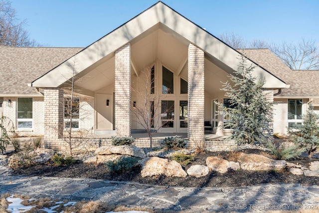 exterior space featuring french doors, brick siding, and a shingled roof