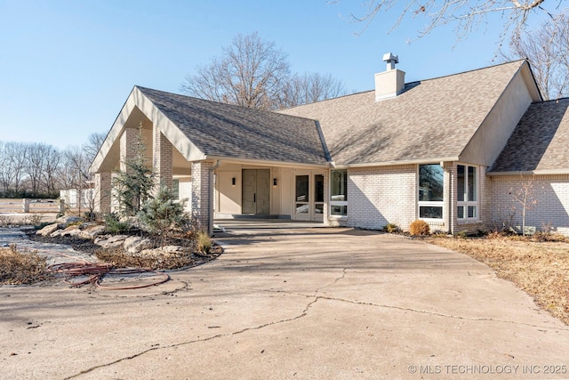 view of front of property with roof with shingles, brick siding, and a chimney