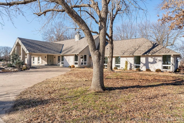 view of front facade with a shingled roof, concrete driveway, brick siding, and a chimney