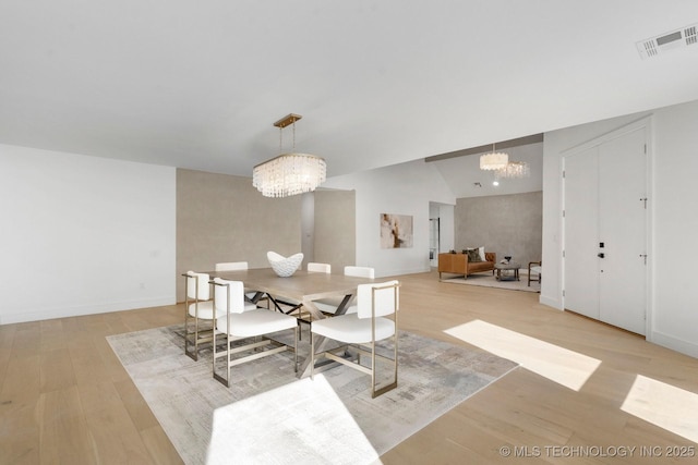 dining space with visible vents, baseboards, vaulted ceiling, light wood finished floors, and an inviting chandelier