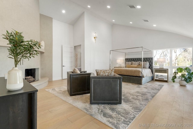 bedroom with high vaulted ceiling, a premium fireplace, light wood-type flooring, and recessed lighting