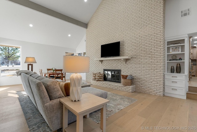 living room with a brick fireplace, visible vents, light wood-style floors, and high vaulted ceiling