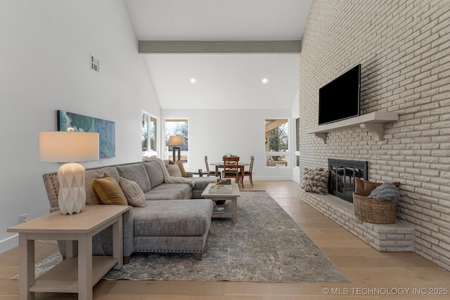 living area with a healthy amount of sunlight, a brick fireplace, beam ceiling, and wood finished floors