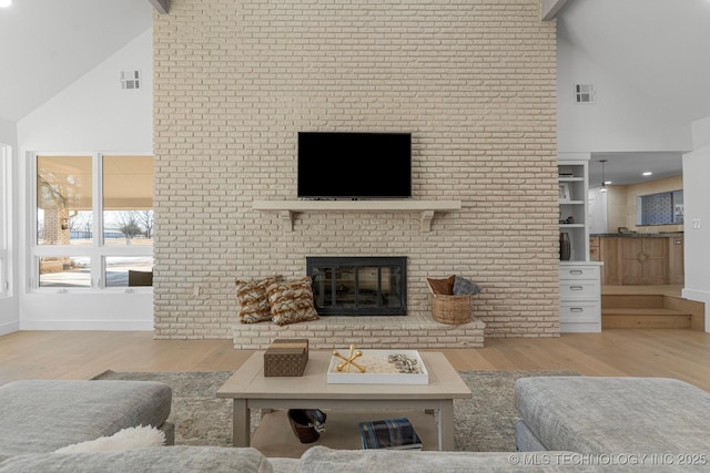 living area featuring high vaulted ceiling, a brick fireplace, visible vents, and wood finished floors