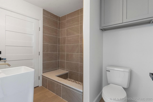 full bath with toilet, a sink, tiled shower, and wood finished floors