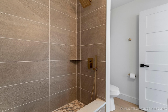 bathroom featuring tiled shower, toilet, and baseboards