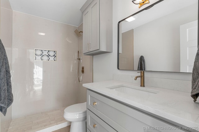 bathroom featuring toilet, a tile shower, and vanity