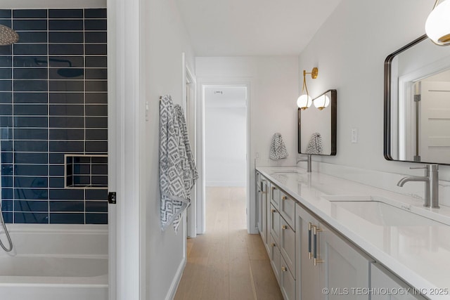 bathroom featuring double vanity, bathing tub / shower combination, a sink, and wood finished floors