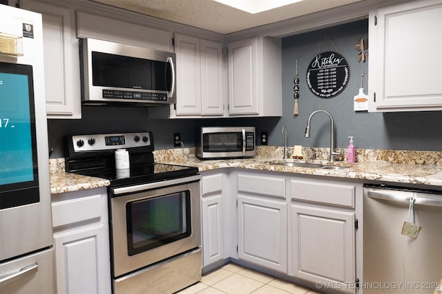 kitchen featuring light tile patterned floors, a sink, white cabinets, appliances with stainless steel finishes, and light stone countertops