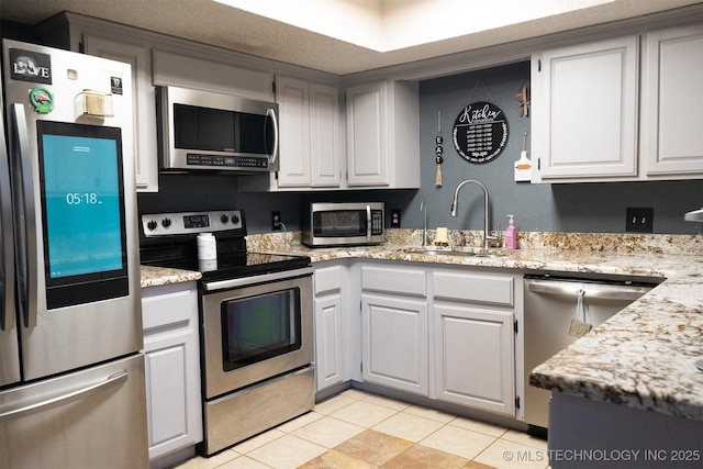 kitchen with light tile patterned floors, appliances with stainless steel finishes, white cabinets, a sink, and light stone countertops