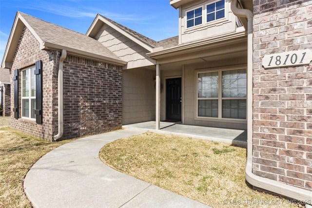 doorway to property featuring a patio area, brick siding, and roof with shingles