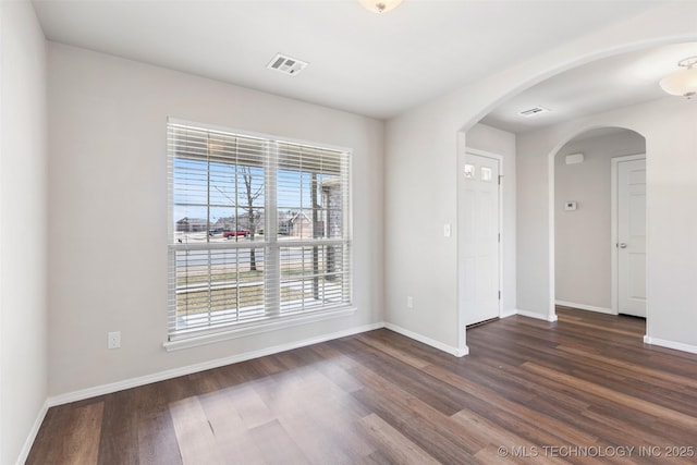 unfurnished room with arched walkways, visible vents, dark wood finished floors, and baseboards