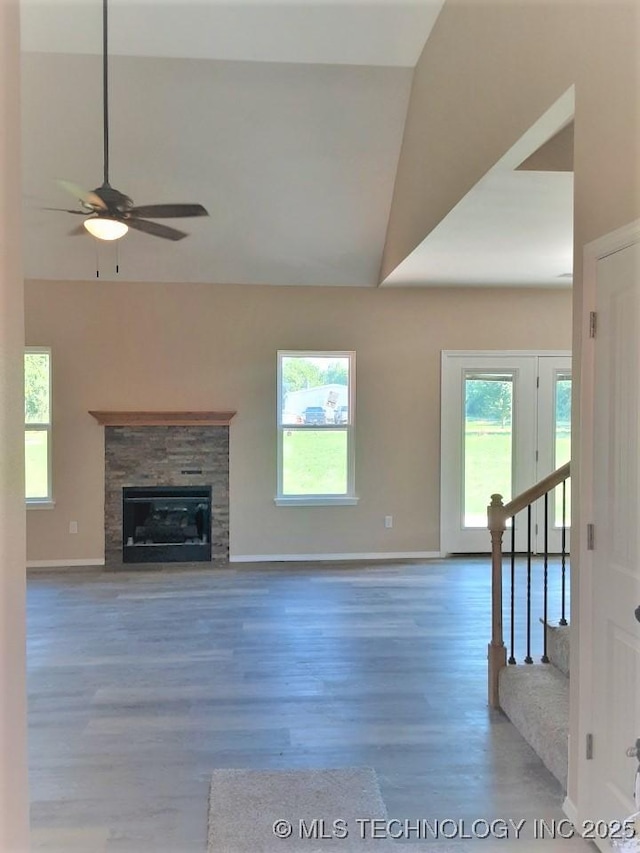 unfurnished living room with stairs, a fireplace, wood finished floors, and a wealth of natural light