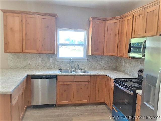 kitchen with light wood finished floors, appliances with stainless steel finishes, backsplash, and a sink