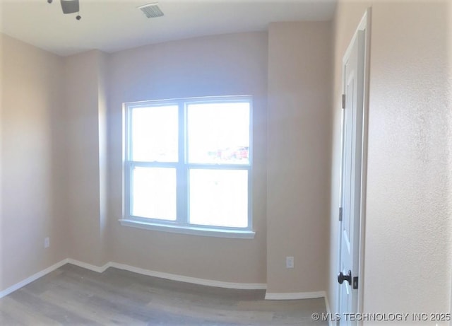 spare room featuring baseboards, visible vents, and wood finished floors