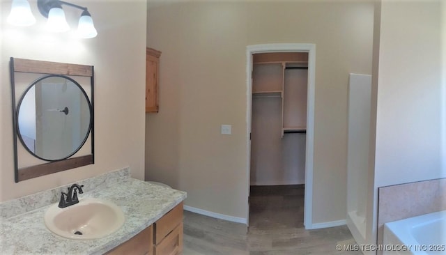 bathroom with wood finished floors, vanity, baseboards, a bath, and a walk in closet