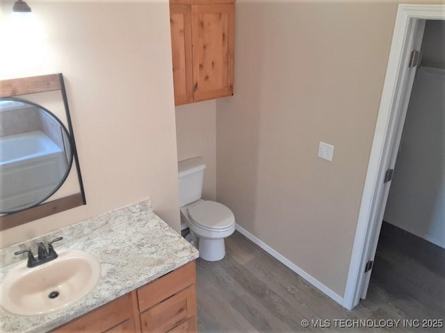 bathroom with toilet, vanity, baseboards, and wood finished floors