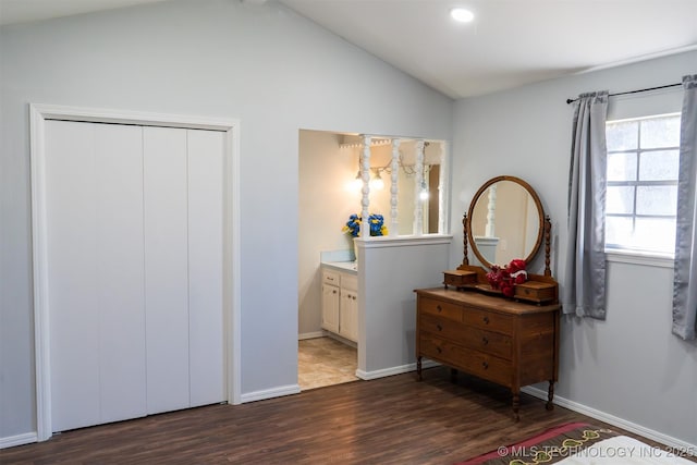 bedroom with lofted ceiling, connected bathroom, wood finished floors, baseboards, and a closet