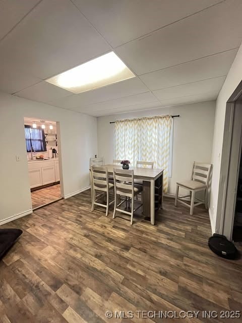 dining area featuring a paneled ceiling, dark wood-style floors, and baseboards