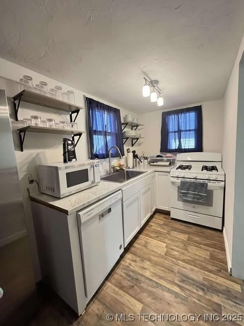 kitchen with open shelves, light countertops, a sink, wood finished floors, and white appliances