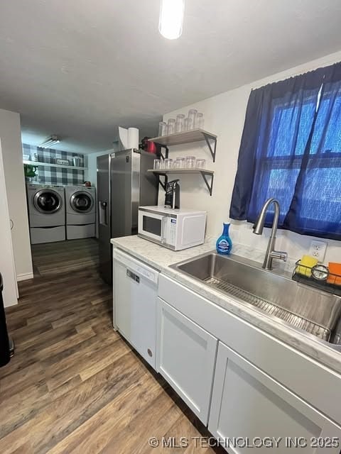 kitchen featuring dark wood-style flooring, washing machine and clothes dryer, open shelves, a sink, and white appliances