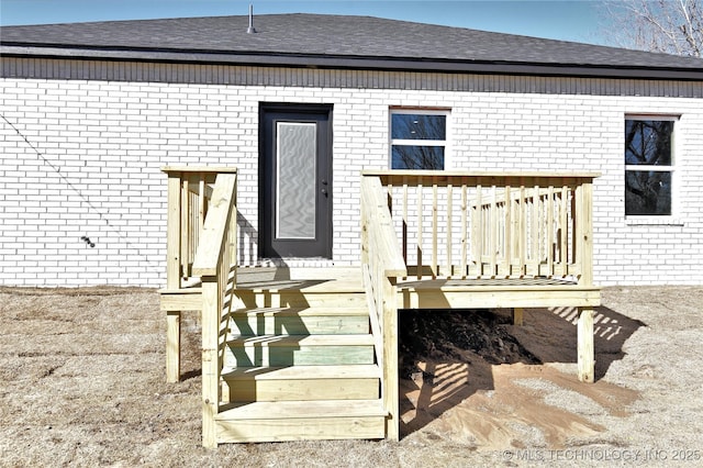 rear view of property featuring brick siding, a shingled roof, and a wooden deck