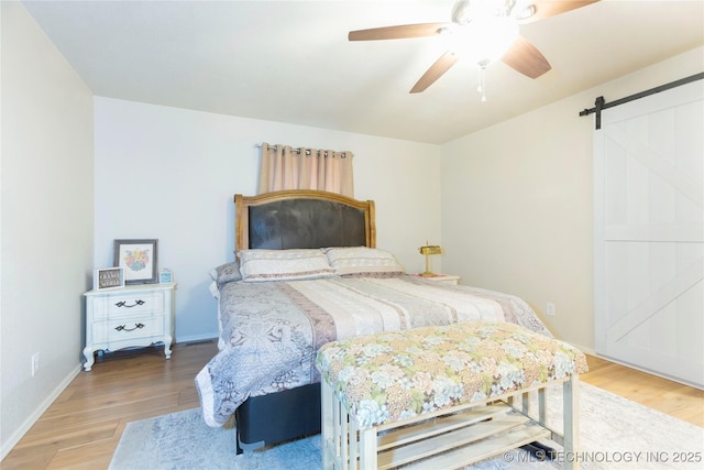 bedroom featuring baseboards, a barn door, light wood-style flooring, and a ceiling fan