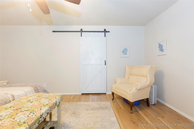 bedroom with a ceiling fan, baseboards, light wood finished floors, and a barn door