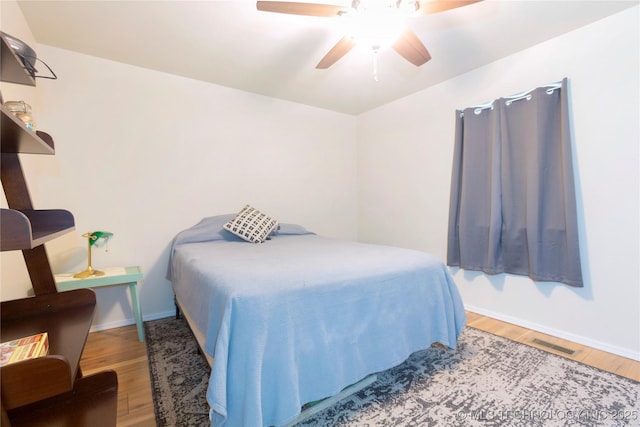 bedroom featuring baseboards, ceiling fan, visible vents, and wood finished floors