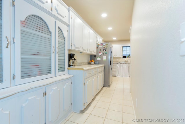 kitchen with white cabinetry, freestanding refrigerator, light countertops, and light tile patterned flooring