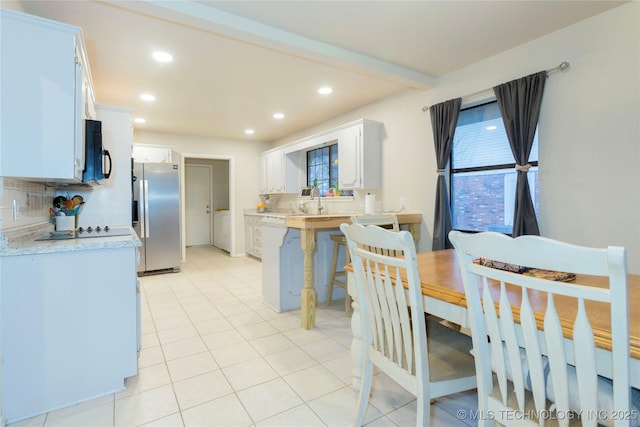 kitchen featuring decorative backsplash, white cabinetry, black microwave, a peninsula, and stainless steel refrigerator