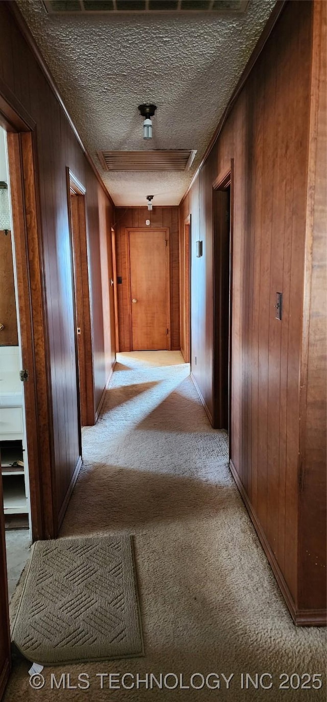 corridor with a textured ceiling, wood walls, and light colored carpet