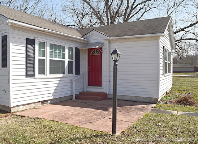 view of exterior entry featuring a shingled roof and a patio area