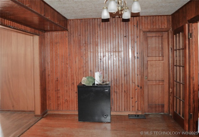 interior space with wood walls, a textured ceiling, wood finished floors, a chandelier, and baseboards