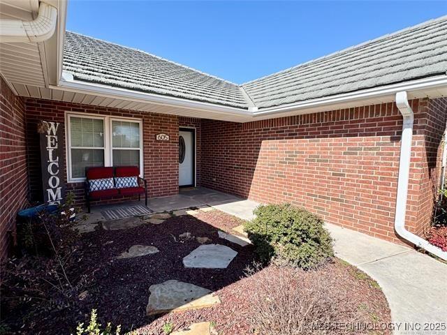 doorway to property featuring brick siding and a tiled roof