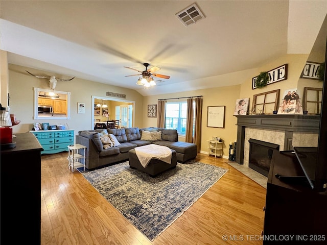 living area featuring visible vents, lofted ceiling, a fireplace, ceiling fan, and light wood-style floors