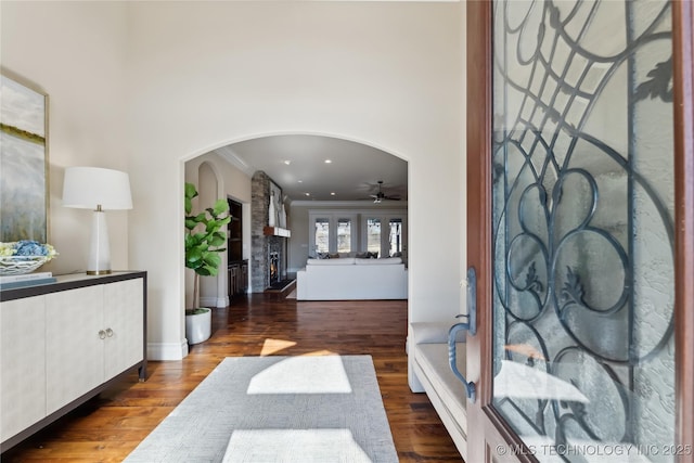 entrance foyer with arched walkways, ceiling fan, wood finished floors, crown molding, and a fireplace