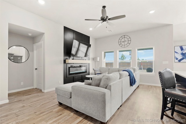 living area featuring a large fireplace, light wood-style flooring, and baseboards