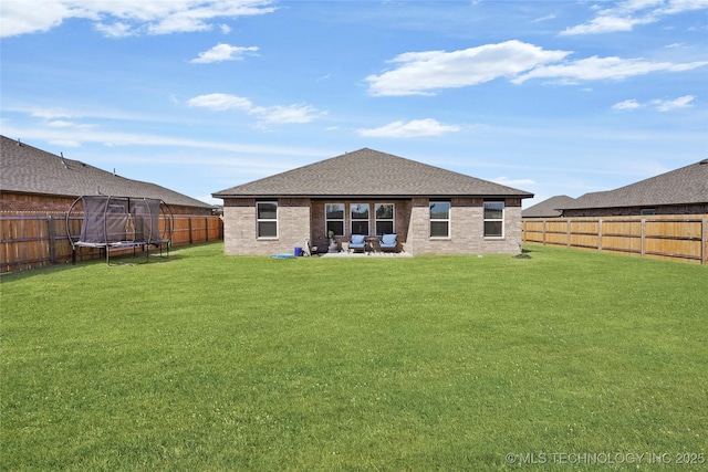 rear view of property featuring a trampoline, brick siding, a yard, a patio, and a fenced backyard