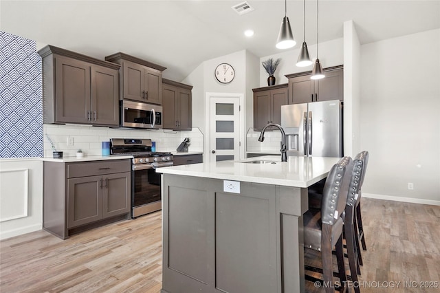 kitchen with decorative backsplash, lofted ceiling, appliances with stainless steel finishes, light countertops, and a sink