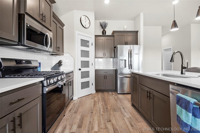 kitchen featuring stainless steel appliances, light countertops, light wood-style flooring, decorative backsplash, and a sink